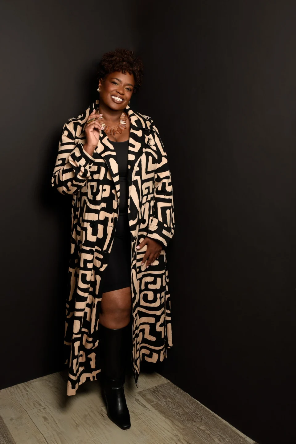 Smiling portrait in a patterned coat against a dark studio backdrop